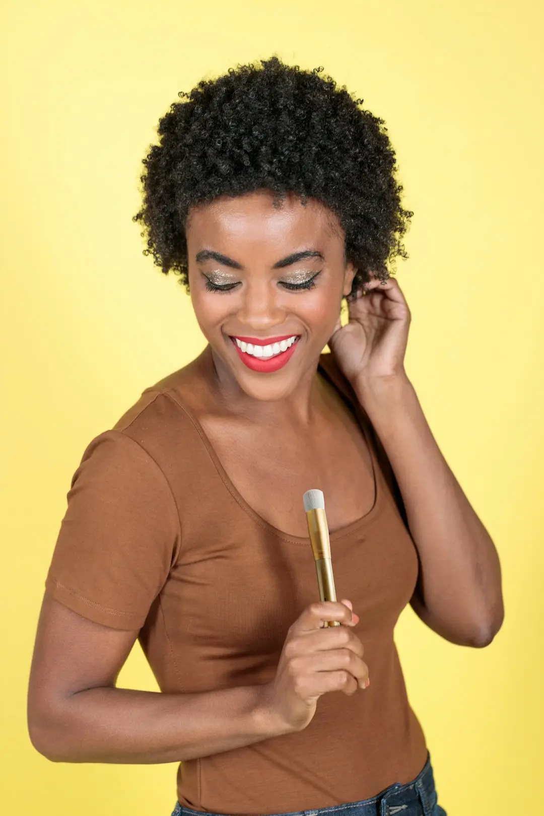 Mulher negra aplicando corretivo em ponto pequeno do rosto diante do espelho, luz natural