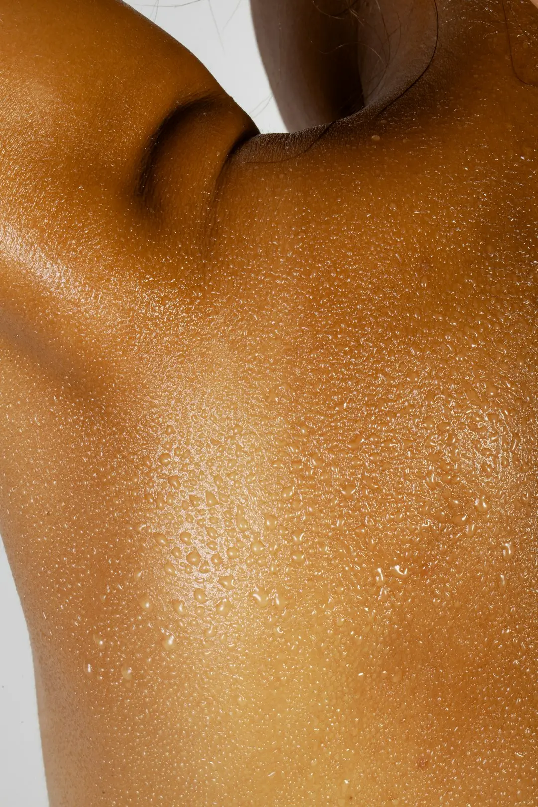 Gotas de óleo corporal escorrendo no braço de pele morena, brilho suave